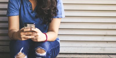 woman sitting at wall looking at phone